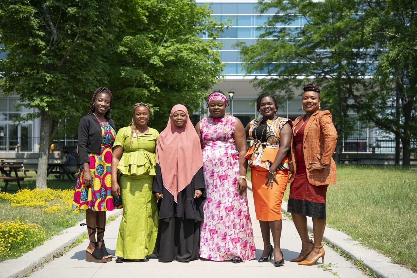 A group of women pose for a photo on a pathway leading to a building with glass windows.