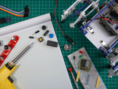 Electronics, tools and robotic supplies lay on a notepad and grid table.