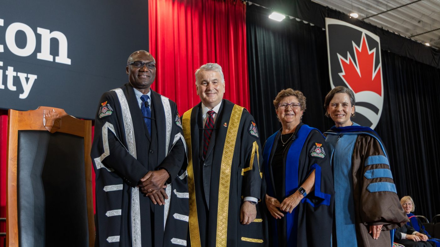A group of four pose for a photo on a convocation stage.