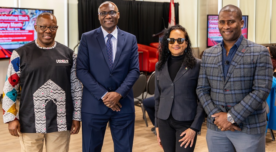 Four professionally dressed academics pose for a group photo.