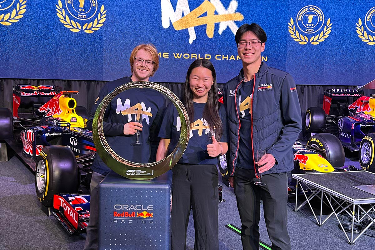 Three people posing with a trophy in front of race cars.