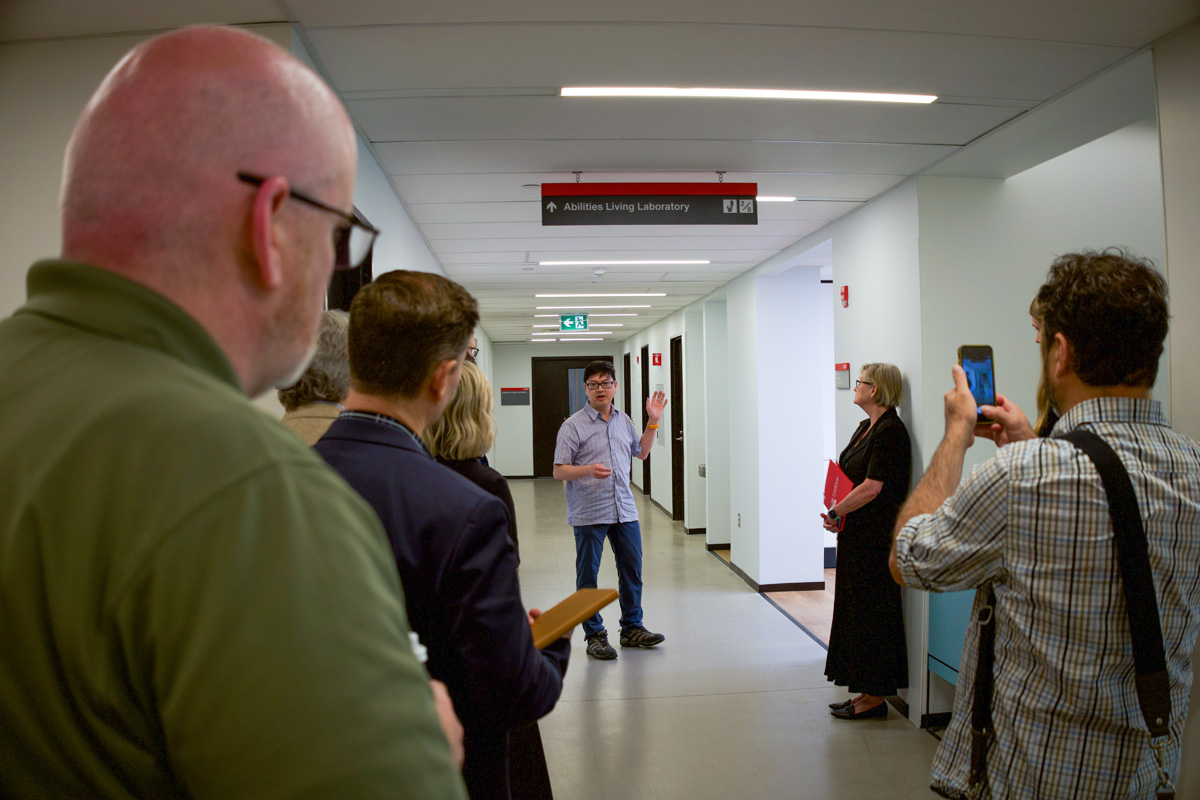 A crowd gathers around a professionally dressed man giving a presentation in a university hallway.