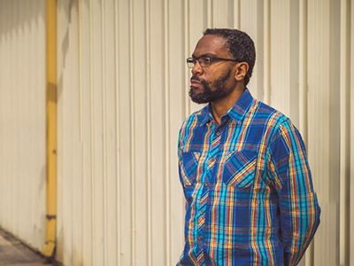 A man in a plaid shirt looks away from the camera while posing for a picture.