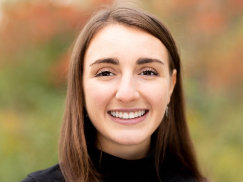 A headshot of a woman with brown hair and brown eyes who is smiling for the camera