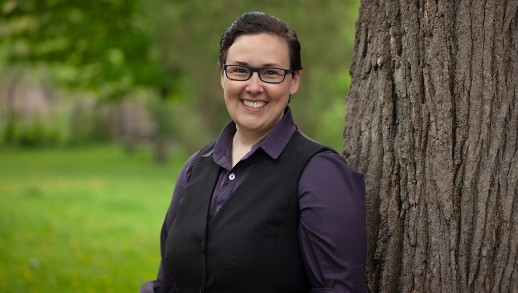 A person with glasses and a suit vest poses for a photo in front of a tree.