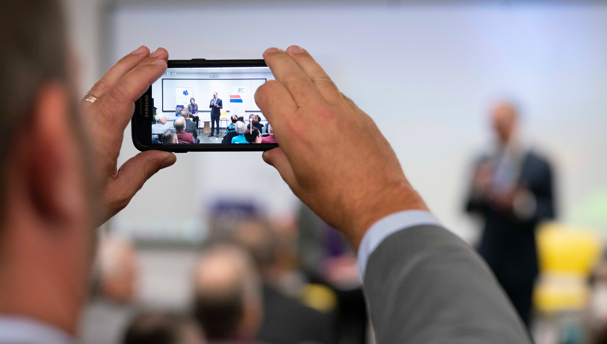 An attendee takes a picture with their mobile phone while Political Science Prof. Joan DeBardeleben puts questions to Niels Annen during Beyond Brexit: The Future of the European Union.