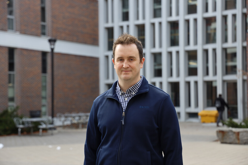 A man in a blue jacket poses for a picture outside an office building.