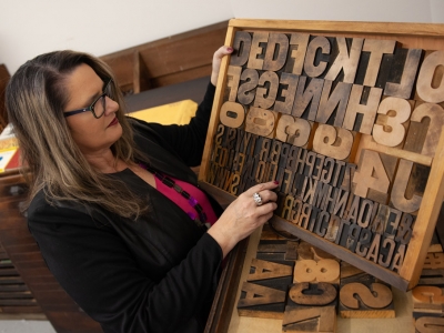 Patti Harper holds a box full of typeset letters in various fonts and sizes.