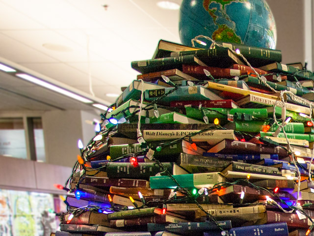 A Christmas tree made of books with a globe on top sits in the MacOdrum Library lobby.