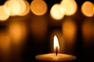 A small candle burns, light from other candles can be seen in the background.