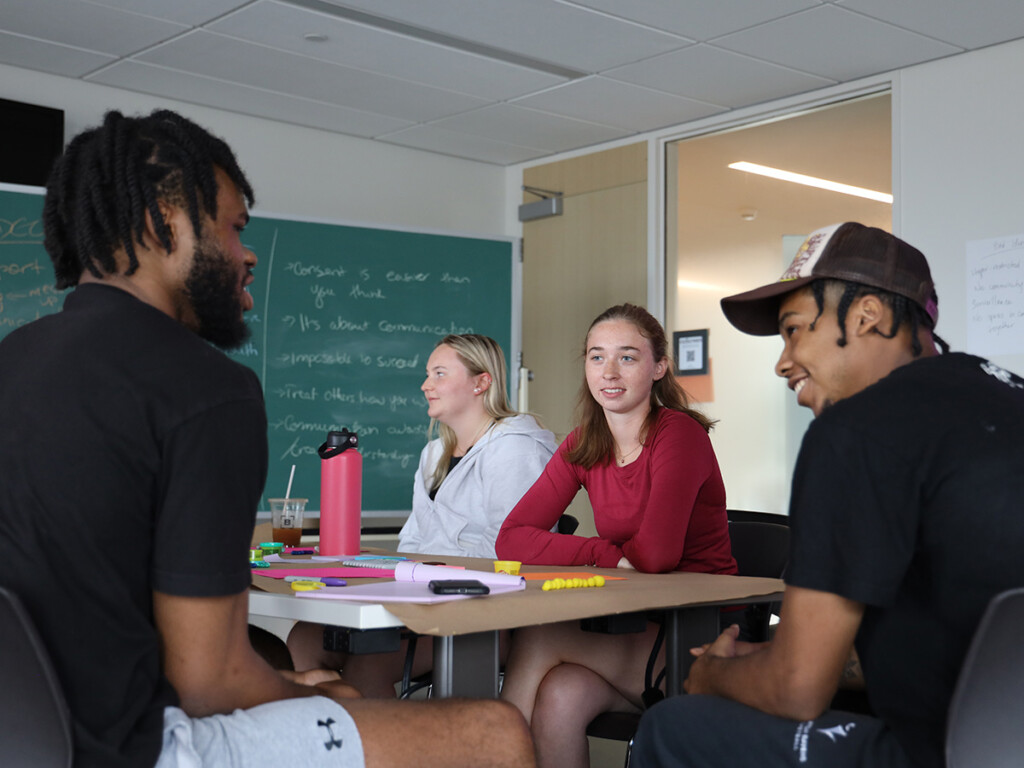 Three young people sitting at desks in a classroom, and having a conversation during a Champions for Change session.