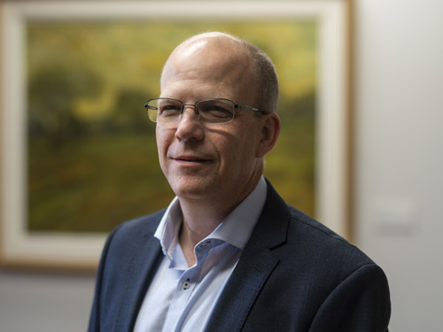 Christopher Worswick poses with a painting hanging on a wall in the background.