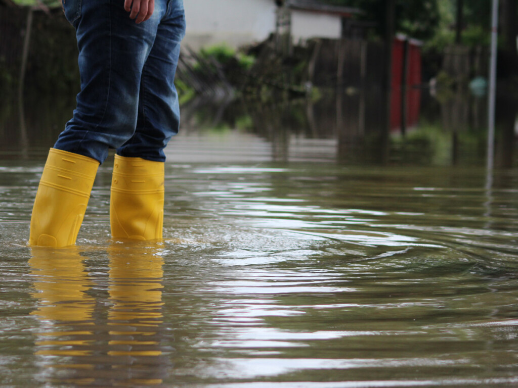 A person in rain boots walks down a flooded street.