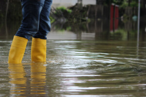 A person in rain boots walks down a flooded street.