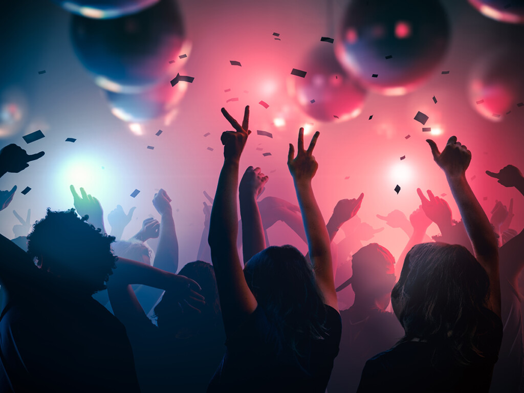 The view from a crowd at a concert; fans cheer with their arms raised