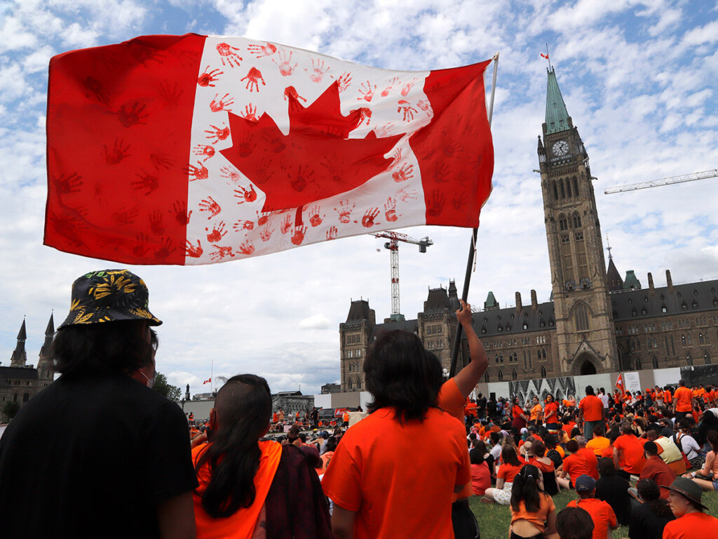 Protesters wave a flag at Parliament Hill in Ottawa at a 'Cancel Canada Day' protest in response to the discovery of hundreds of unmarked graves at Indian Residential Schools. (THE CANADIAN PRESS/ Patrick Doyle)