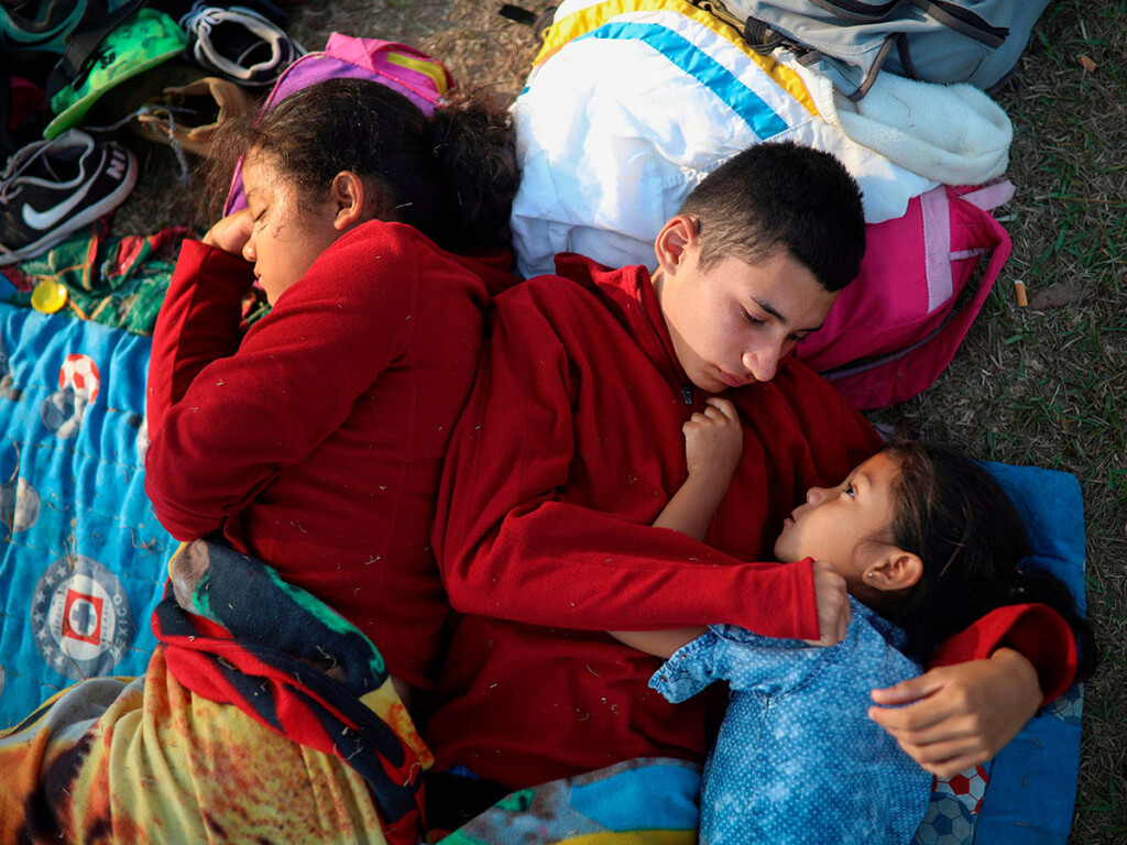 In this April 2018 photo, siblings from El Salvador huddle together on a soccer field in Mexico. awaiting temporary transit visas that would allow them to continue to the U.S. border, where they hoped to request asylum. (AP Photo/Felix Marquez)