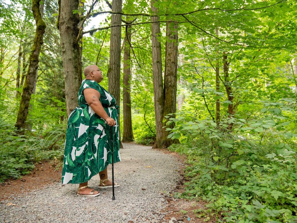 A woman walks with a cane down a forest pathway.