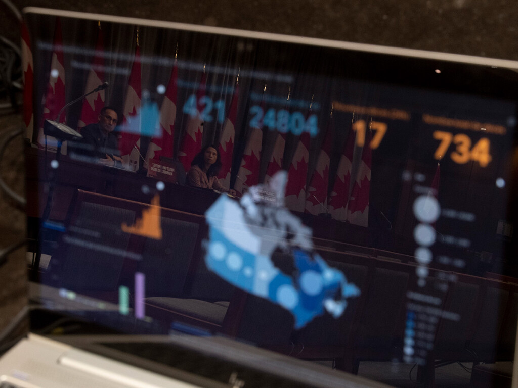 Chief Public Health Officer Theresa Tam and Deputy Chief Public Health Officer Howard Njoo are reflected in a computer screen showing date on Canada's COVID-19 situation during a news conference in Ottawa, on April 13, 2020. (THE CANADIAN PRESS/Adrian Wyld)