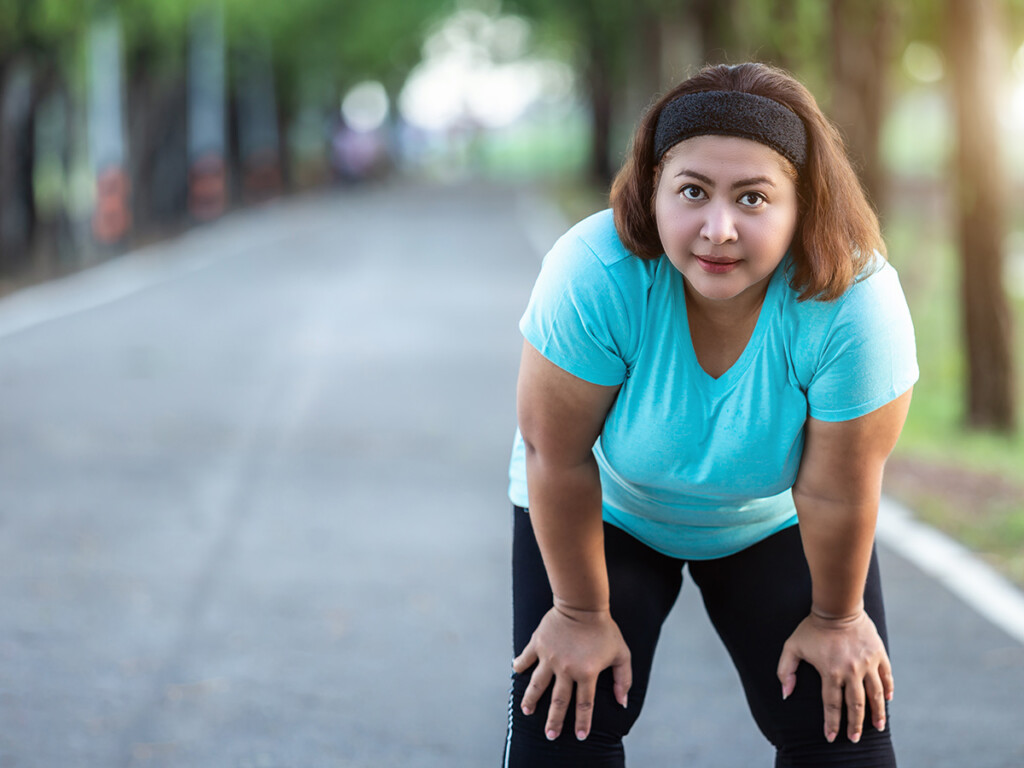 A woman leans over and rests her hands on her knees to takes a break from physical activity