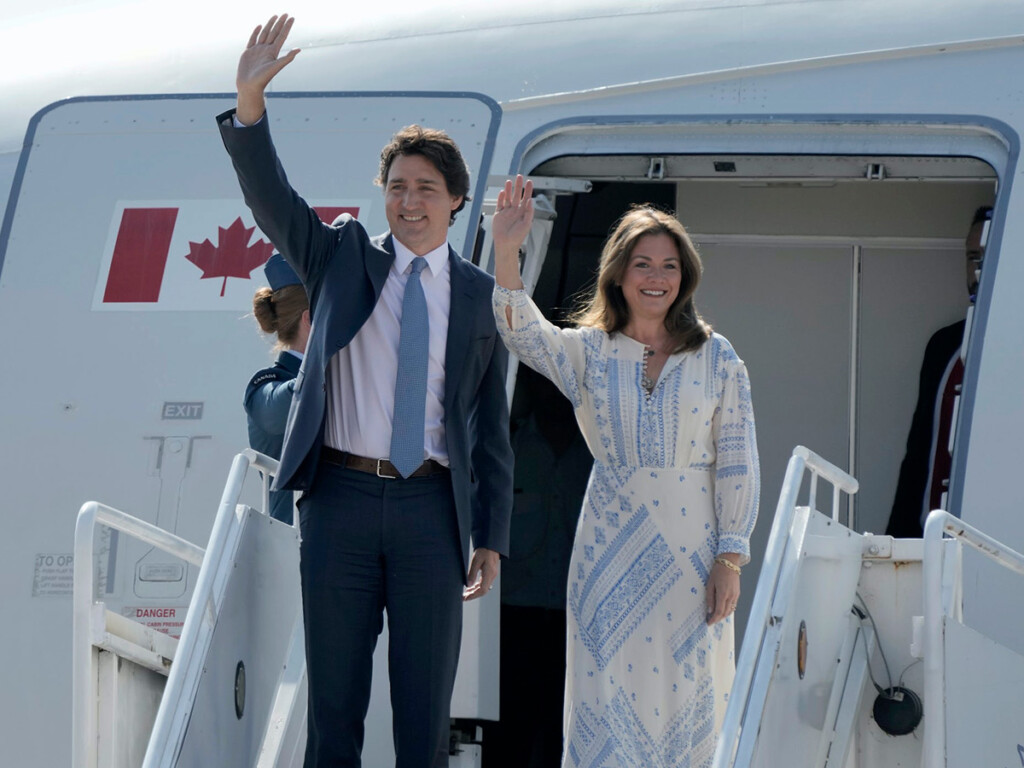Justin Trudeau and Sophie Grégoire Trudeau wave to onlookers while boarding an airplane which has a Canadian flag on the door.