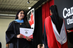 A graduate receives a degree on stage as Carleton Celebrates Fall Graduates