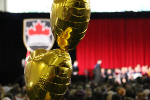 Balloons float in the Fieldhouse as a crowd watches graduates receive their cu_people_degree on stage.