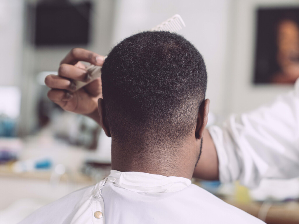 A black man gets his hair cut in a barbershop.