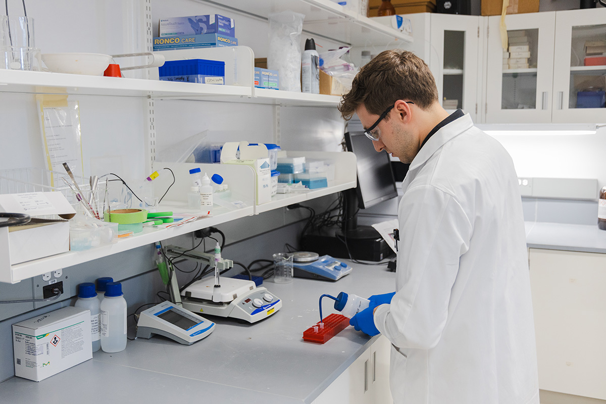 A scientist wearing a lab coat and safety goggles, creates a sample of a specimen inside a laboratory.
