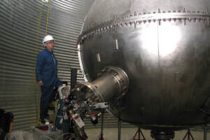 A man in a blue safety suit and white hard hat examines a large piece of equipment used for researching dark matter.
