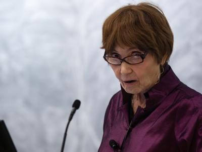 Elizabeth Abbott speaks into a microphone in an auditorium.