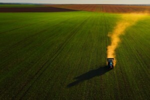 A tractor fertilizes a wheat field from an aerial view