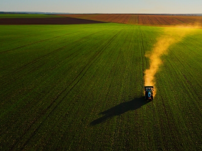 A tractor fertilizes a wheat field from an aerial view