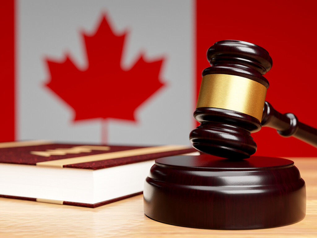 A gavel sits on a table next to a book with the Canadian flag visible on the wall in the background.