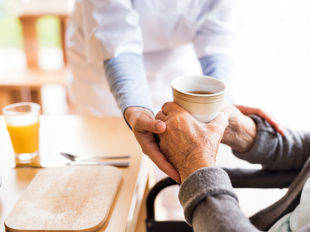 The hands of a nurse can be seen holding the hands of an elder patient.