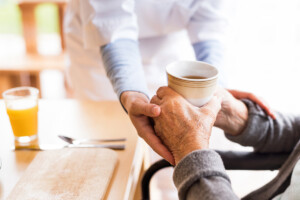 The hands of a nurse can be seen holding the hands of an elder patient.