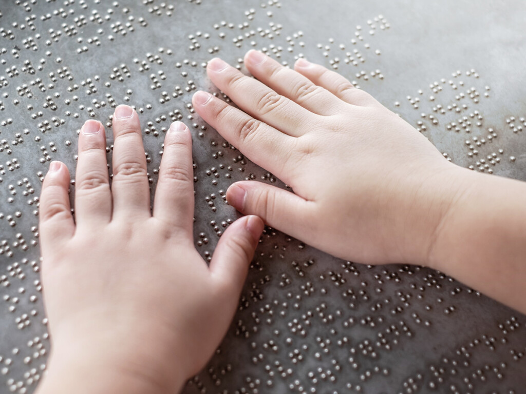 The hands and fingers of a young child touching Braille letters