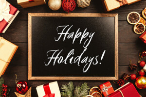 A chalkboard with the words Happy Holidays! Gifts and oranaments wrap the border of the image.