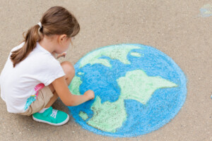 a child girl draws a planet of the world with colored chalk on the asphalt. Children's drawings, paintings and concepts. Education and art, be creative when you return to school.