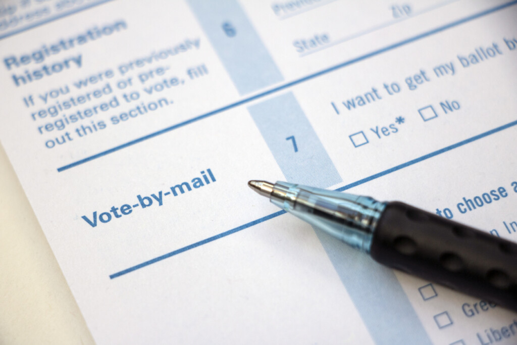 Closeup of 'Vote-by-mail' section on a voter registration form, with ballpoint pen laying on the form.