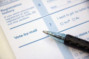 Closeup of 'Vote-by-mail' section on a voter registration form, with ballpoint pen laying on the form.