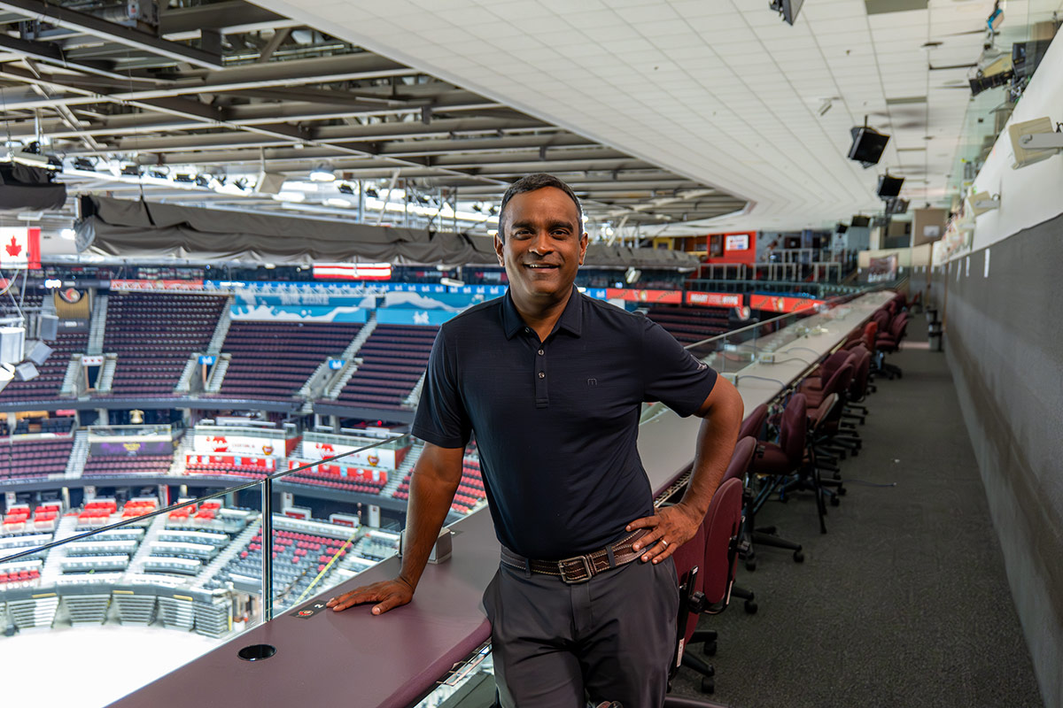 A professionally dressed man leans against a railing inside a hockey arena.