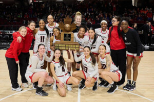 A championship winning basketball team posing on the court with a large trophy.