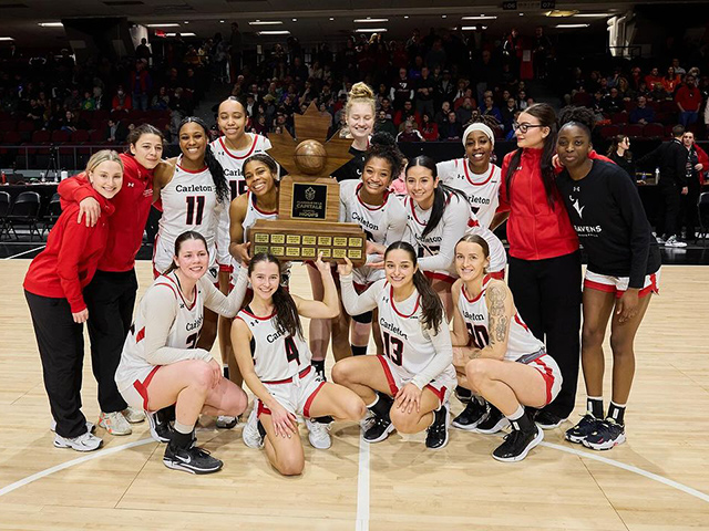 A championship winning basketball team posing on the court with a large trophy.