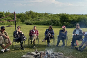 A group of people sitting outside around a fire pit.