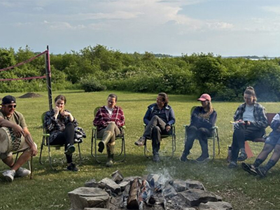 A group of people sitting outside around a fire pit.