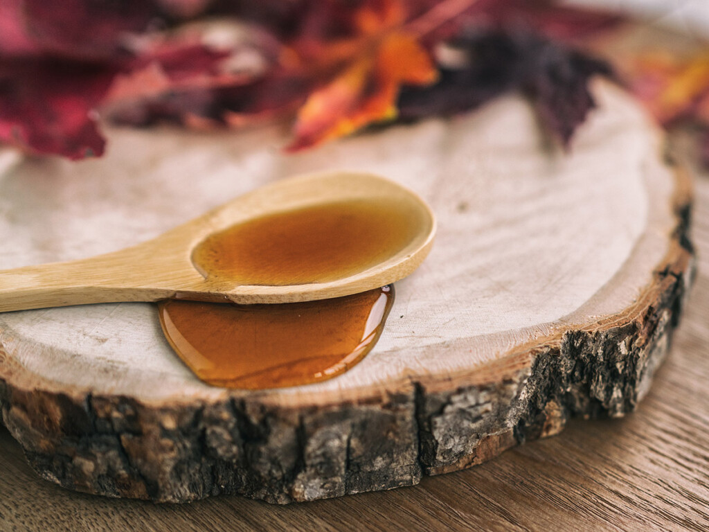 A spoon covered in maple syrup, sitting on a log.