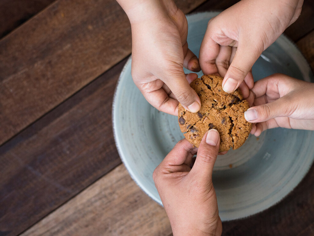 Four hands splitting a cookie four ways, to represent the Cookie Challenge on TikTok.