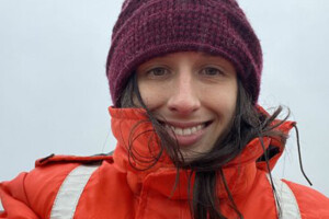 A woman with bright orange jacket and a mauve hat.