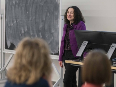 Dr. Kim Corace stands near a podium with a blackboard in the background.